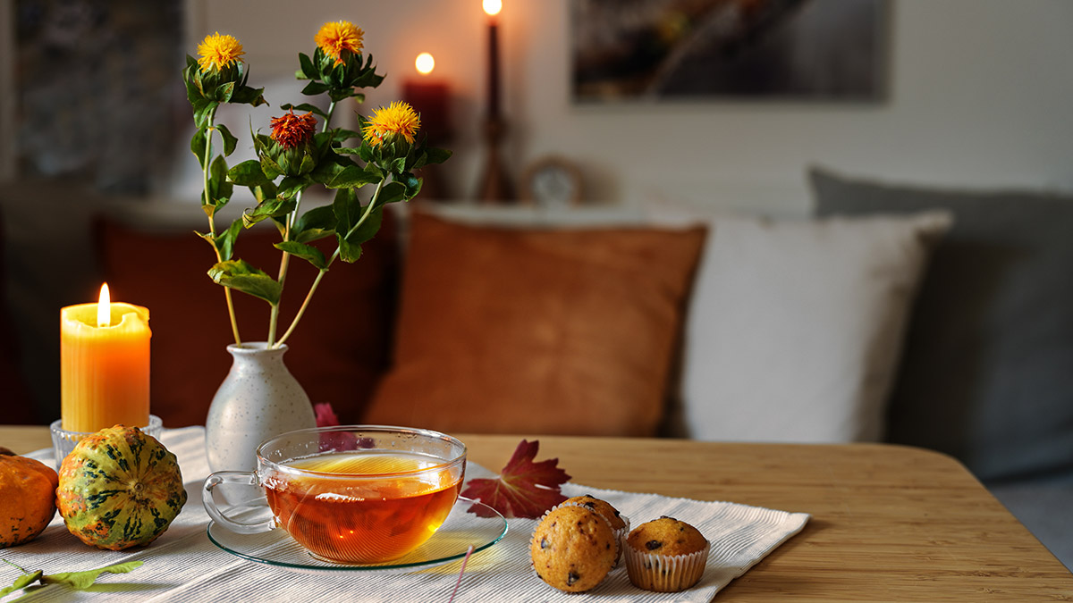 Ein herbstlich gedeckter Tisch mit Tee, Muffins, Blumen und Kerzen.