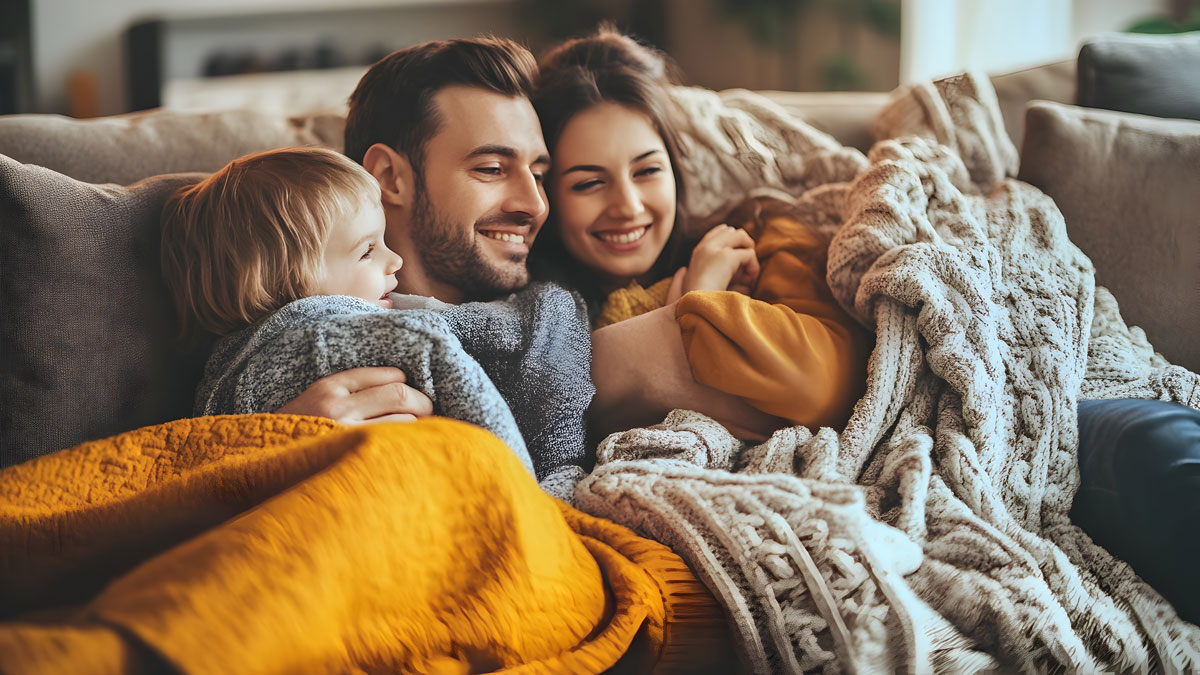 Kuscheldecke Tipps, Mutter, Vater und Tochter unter Kuscheldecken im Herbst auf dem Sofa