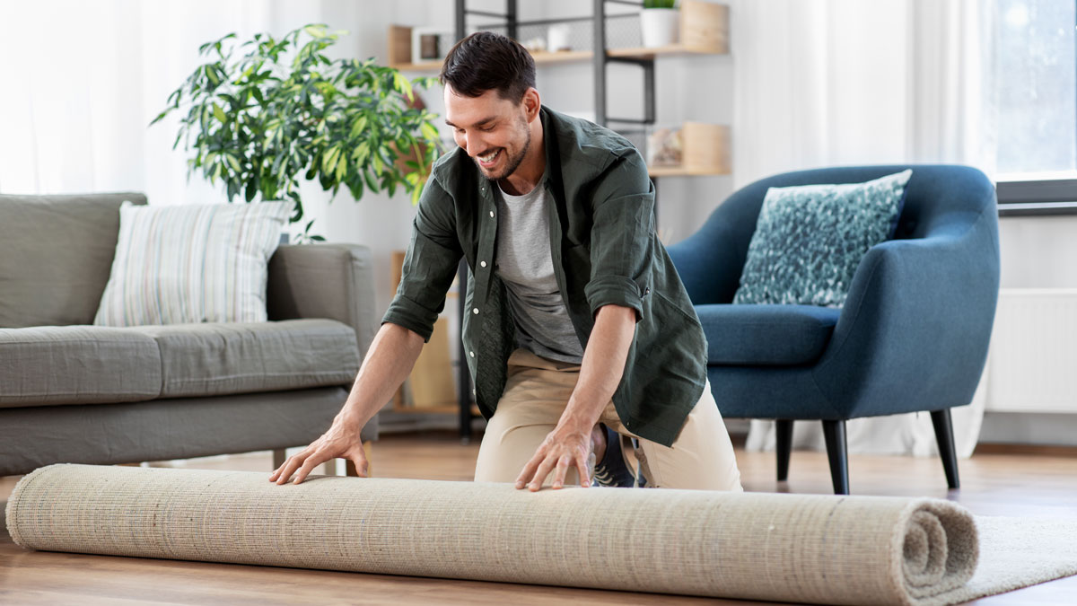 Teppiche Tipps, Mann rollt im Wohnzimmer einen Teppich aus