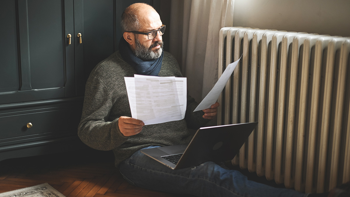 Kalte Nachbarwohnung, Mann sitzt vor seinem Heizkörper und checkt die Heizkostenabrechnung