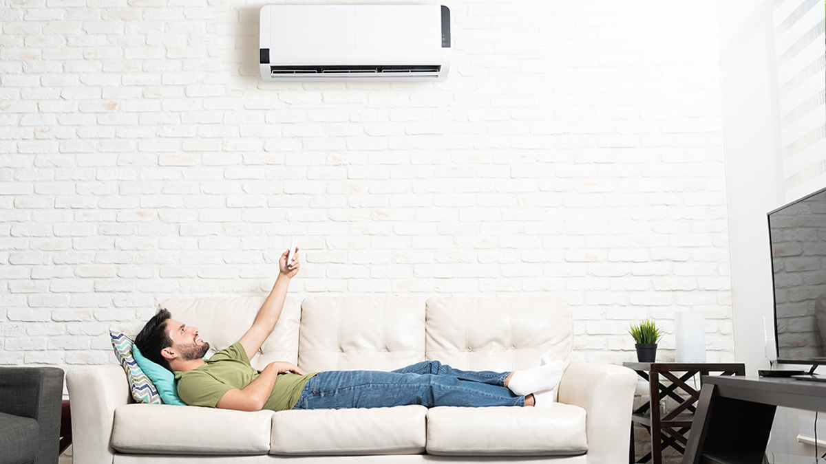 Klimaanlage dynamischer Stromtarif, Mann liegt entspannt am Sofa und schaltet mit Fernbedienung die Klimaanlage ein
