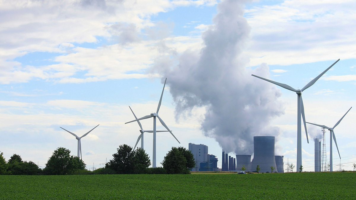 Rückgang Energieverbrauch, Windräder neben einer Industrieanlage mit rauchenden Schornsteinen