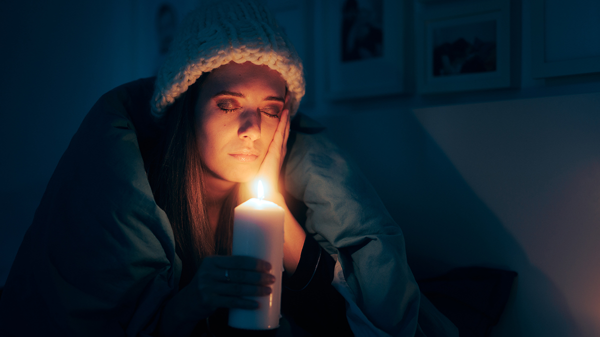 Stromausfall Vorbereitung, Frau sitzt bei Dunkelheit nach Stromausfall mit einer Kerze und Decke in der Wohnung