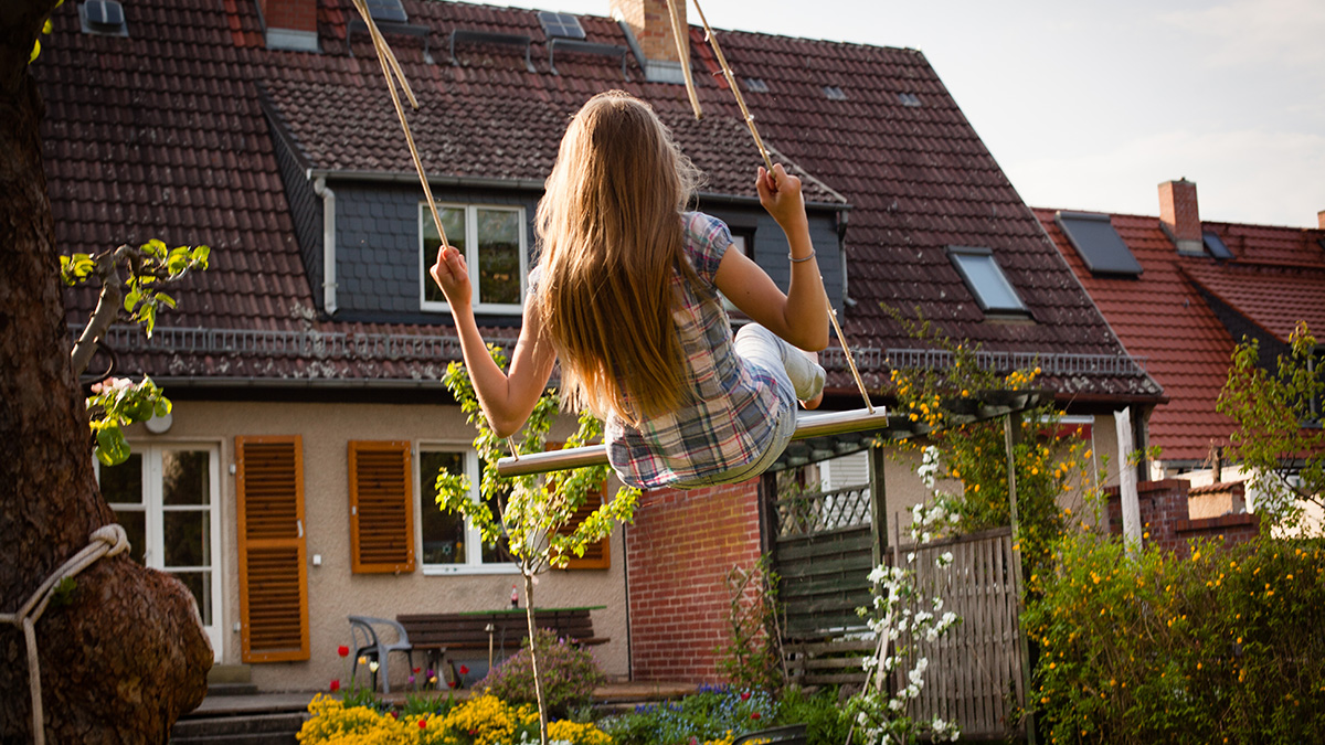 Vergleich Förderungen, Mädchen auf Schaukel im Garten mit Blick auf ein Einfamilienhaus, Foto: iStock.com / fotografixx