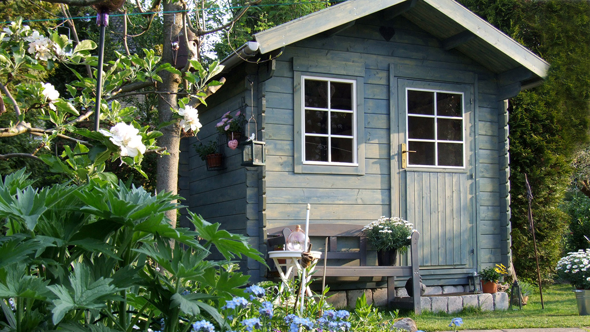 Ein blaues Gartenhaus neben Bäumen und Sträuchern