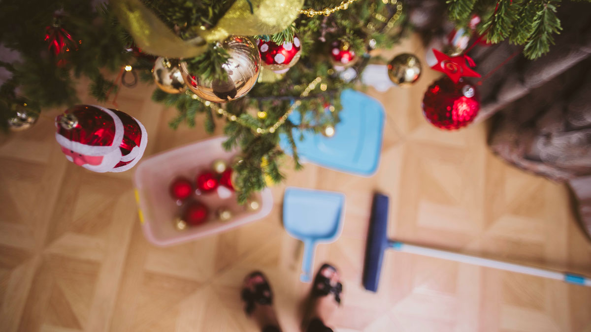 Aufräumtipps nach Weihnachten, Frau hängt die Kugeln vom Weihnachtsbaum und kehrt