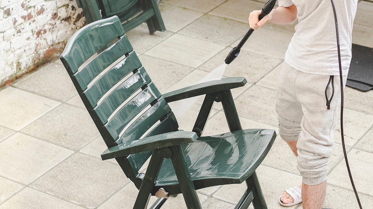 Blütenstaub entfernen, Mann reinigt Gartenstuhl mit Hochdruckreiniger