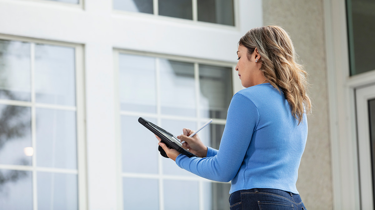 Fehler beim Hauskauf, Frau steht vor einem Haus und macht Notizen, Foto: iStock.com / kali9