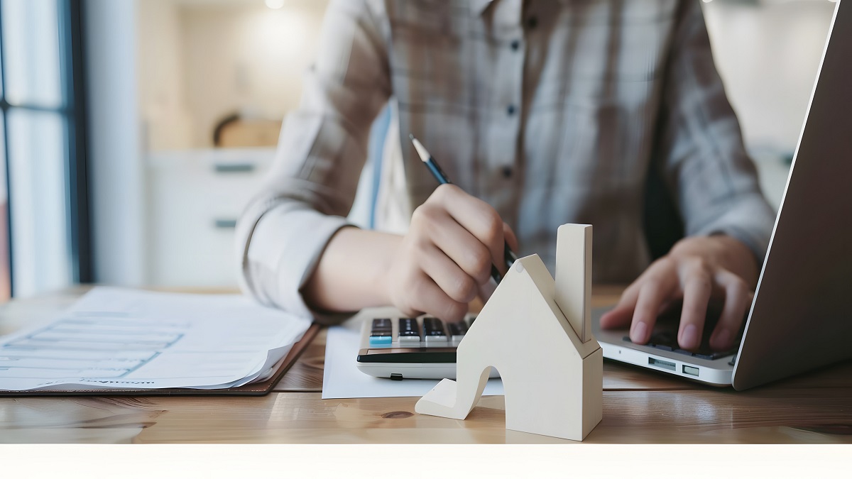 Frau vor Laptop und Miniaturhaus