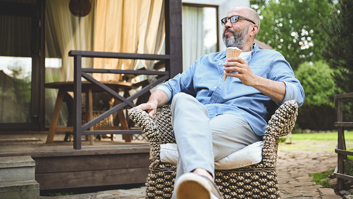 Hauskauf ab 50, Mann über 50 sitzt mit Eis in der Hand in seinem Garten