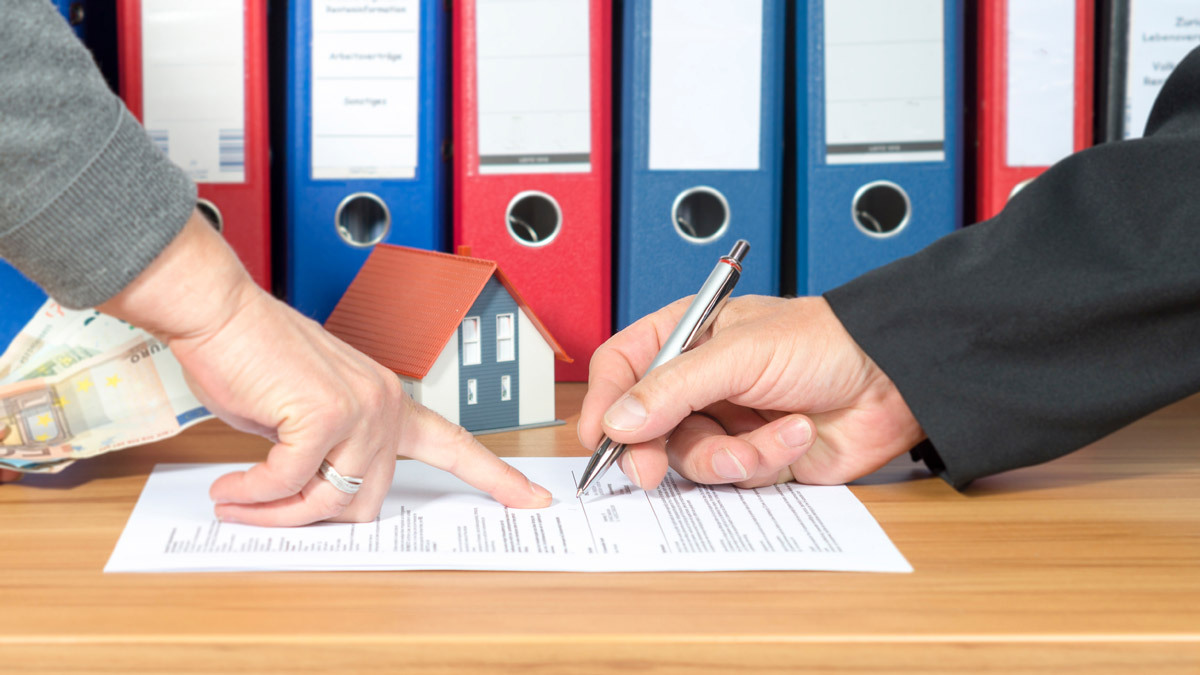Ein Mann unterschreibt einen Vertrag, eine andere Hand zeigt auf das Unterschriftsfeld
