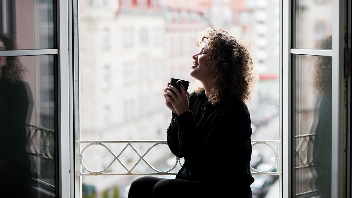 PM AT Sicherheit, Frau trinkt zufrieden einen Kaffee vor offenem Fenster