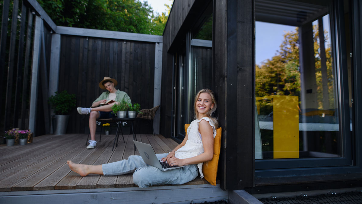Tiny House mieten, junges Paar sitzt zufrieden vor ihrem gemieteten Tiny House