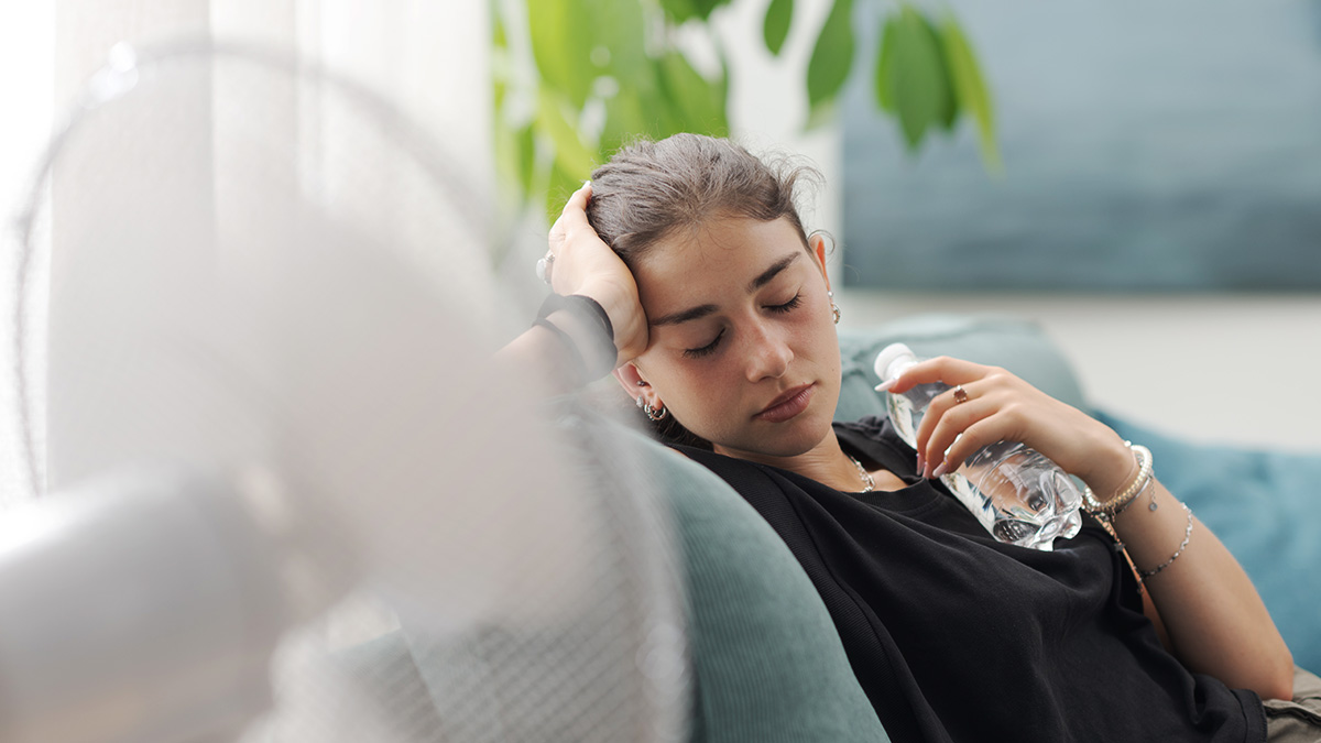 Ideale Raumtemperatur im Sommer, Frau schwitzt im Sommer in der Wohnung trotz Ventilator