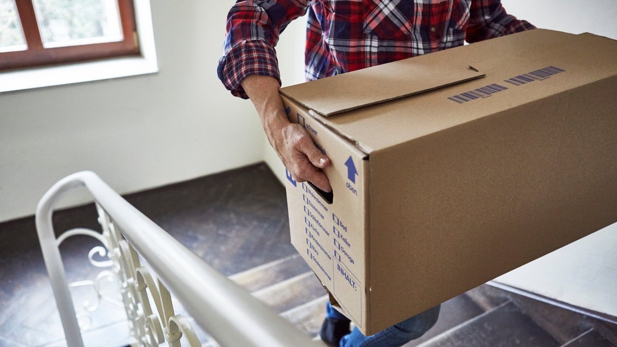 Hausratversicherung Umzug, Person trägt einen großen Umzugskarton über eine Treppe