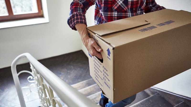 Hausratversicherung Umzug, Person trägt einen großen Umzugskarton über eine Treppe