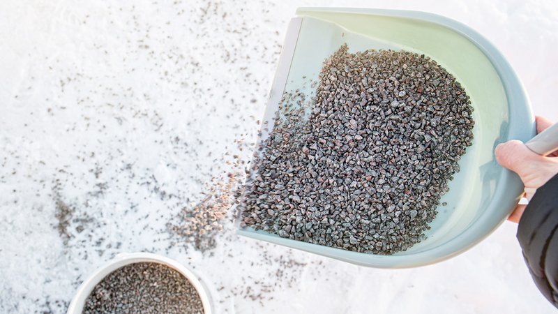 treusalzalternativen, Schaufel mit Split wird auf vereisten Gehweg gestreut