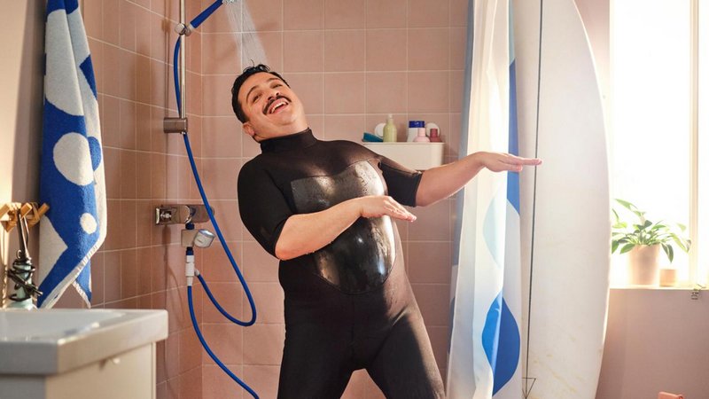 Ein Mann im Badeanzug duscht vergnügt.