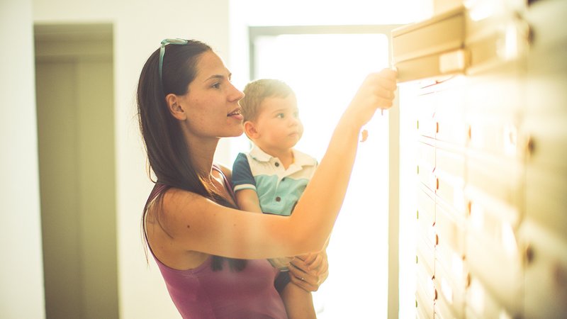 Nachsendeauftrag, Frau mit Kind auf dem Arm öffnet Briefkasten
