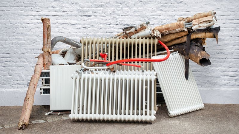 Heizungstausch, alte Heizung und Heizkörper stehen ausgebaut an der Straße