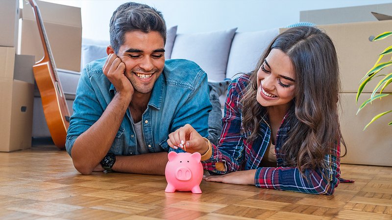 Ein Paar liegt auf dem Boden und steckt eine Münze in ein Sparschwein