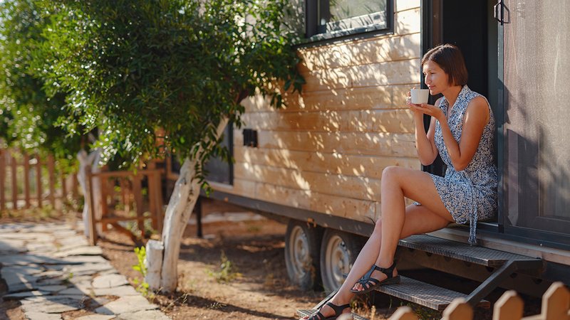 Tiny House nach Scheidung, geschiedene Frau sitzt zufrieden vor ihrem Tiny House und trinkt Kaffee