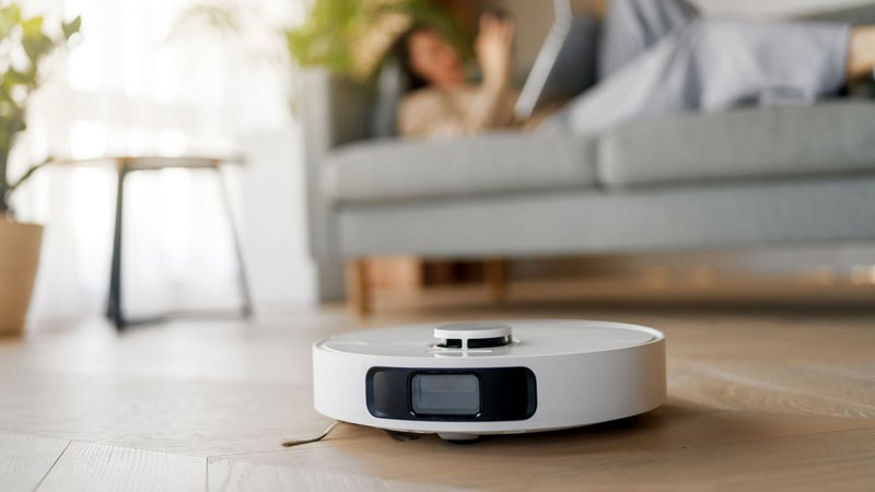 Saugroboter, Frau liegt entspannt auf dem Sofa, während der Saugroboter arbeitet