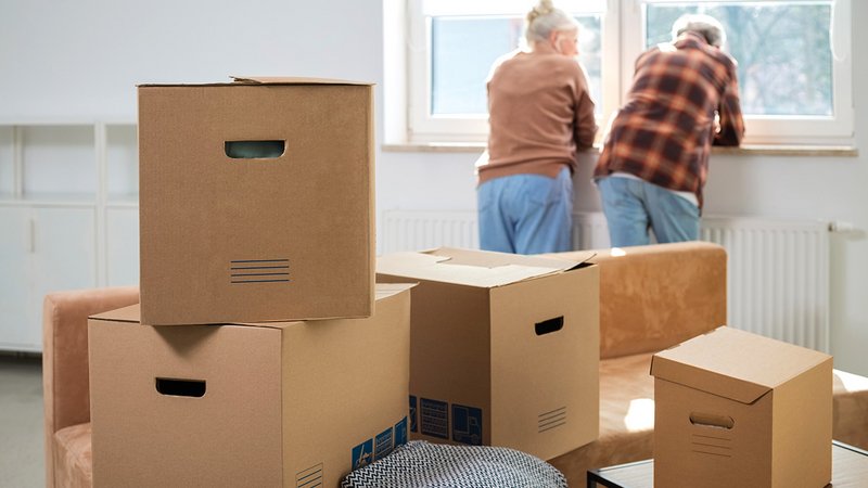 Ein älteres Paar steht am Fenster, um sie herum gepackte Kartons
