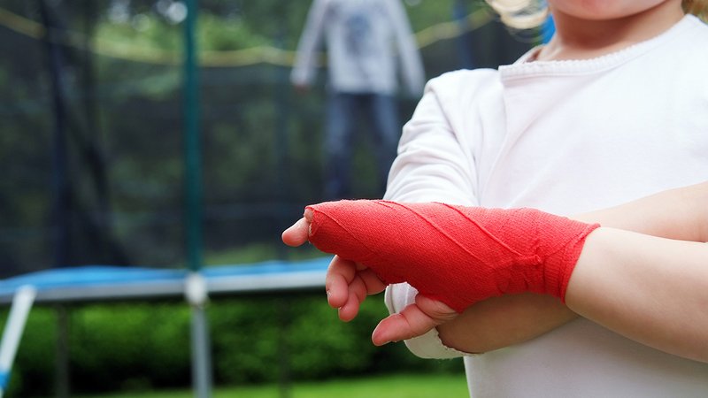 Trampolin im Garten, Kind mit gebrochenem Arm im Verband vor Trampolin