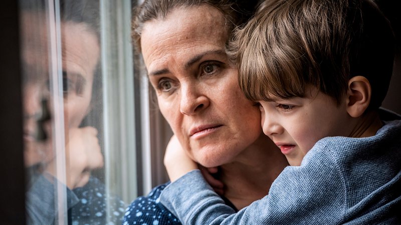 Neue Grundsicherung, Frau mit Sohn auf dem Arm blickt traurig aus dem Fenster
