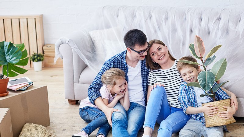 Eine Familie sitzt auf dem Boden vor dem Sofa, der Junge hält eine Pflanze