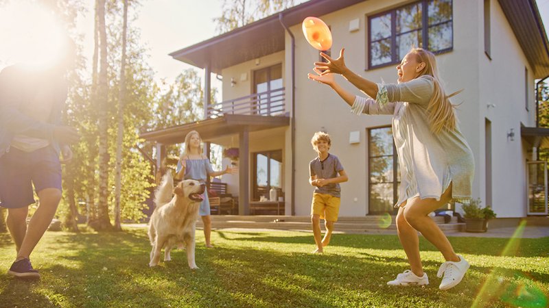 Baufinanzierung mit Eigenkapital, Familie spielt im Garten vorm Eigenheim Frisbee