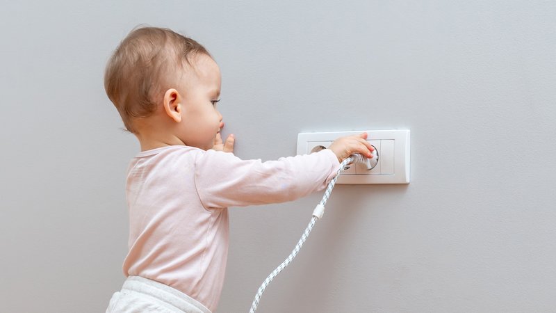 Kleinkind zieht einen Stecker aus einer Steckdose