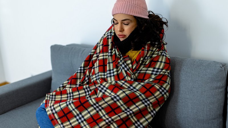 Darf mein Vermieter die Heizung abstellen, frierende Frau mit Decke auf dem Sofa in ihrer Wohnung