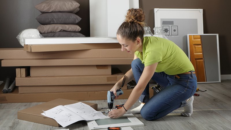 Möbel aufbauen, abbauen, junge Frau kniet auf dem Boden und schraubt ein Regal zusammen