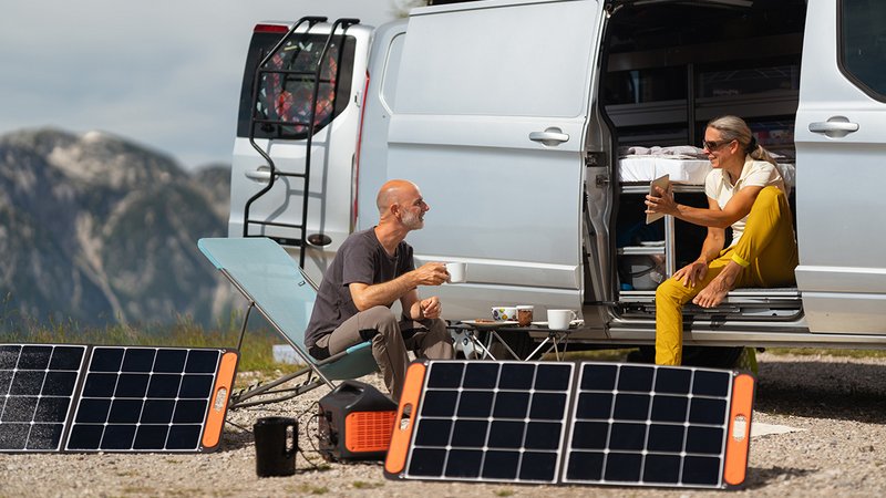 Faltbare PV Anlage, Paar sitzt mit faltbarer PV Anlage vor Van