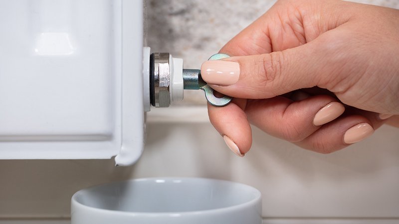 Heizung fit machen, Frau mit lackierten Fingernägeln entlüftet einen Heizkörper