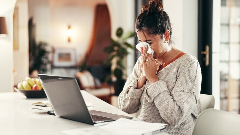 Eine Frau sitzt vorm Laptop und putzt sich die Nase