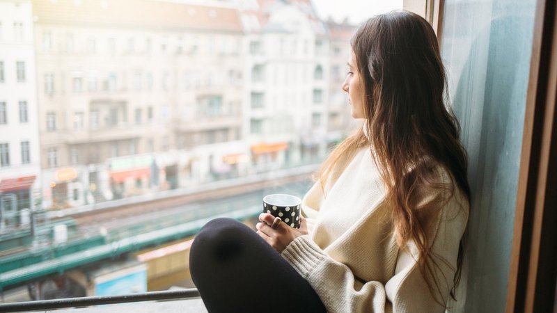 Berlin PM gesunde Mieten, Single-Frau sitz in Berliner Wohnung am Fenster und trinkt Kaffee