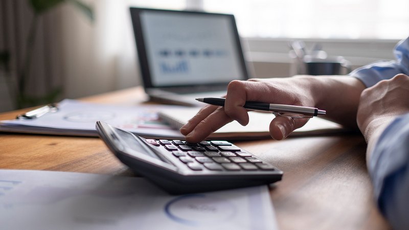Tipps rechtssichere Mieterhöhung, Vermieter sitzt vor seinem Laptop und tippt auf dem Taschenrechner