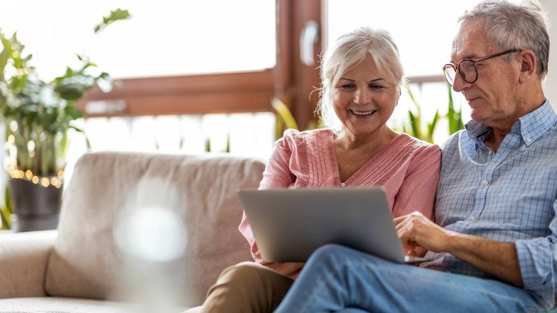 Immobilienkredit Höchstalter, älteres Paar sitzt am Sofa vor Laptop