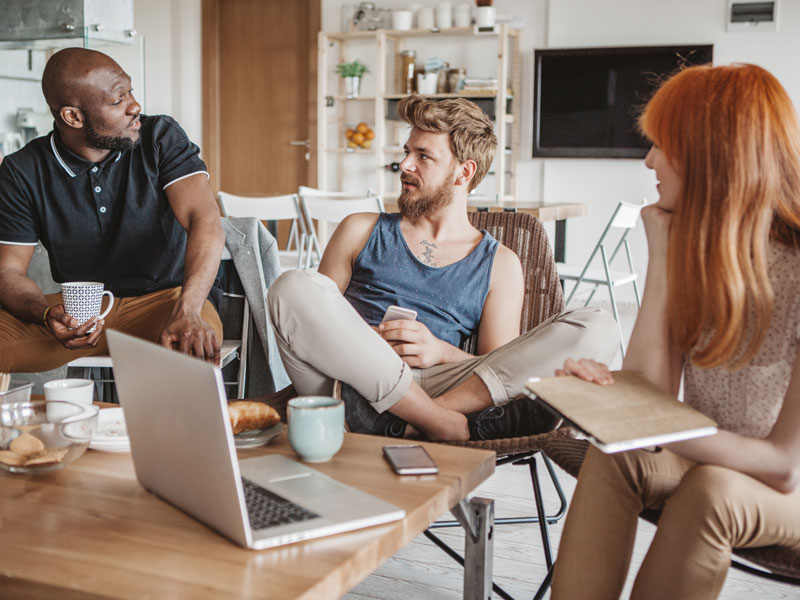 WG-Mietvertrag, Foto von zwei jungen Männern und einer jungen Frau in einem Gemeinschaftsraum beim Unterhalten,