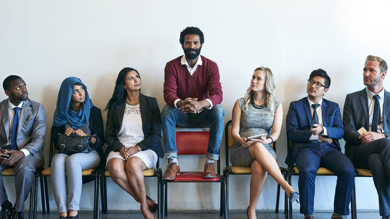 Sieben Menschen sitzen in einer Reihe, in der Mitte ist einer erhöht.