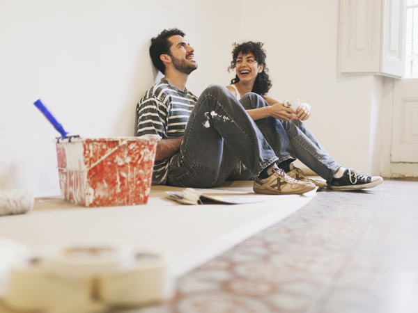 Ein paar sitzt vor einer weißen Wand, den Farbtopf neben sich.