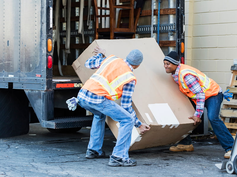 Haushaltsauflösung, Unternehmen, Zwei Männer in Warnwesten laden einen großen Karton in einen Laster