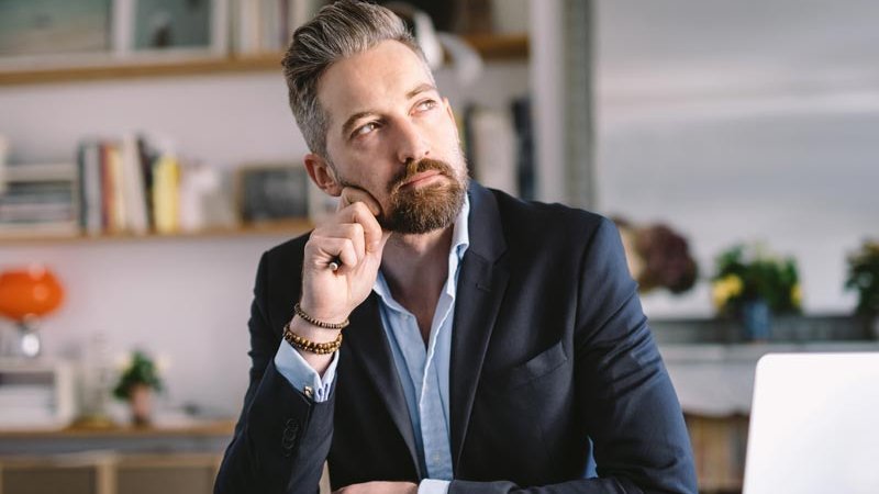 Ein Mann sitzt vor seinem Laptop und denkt nach.