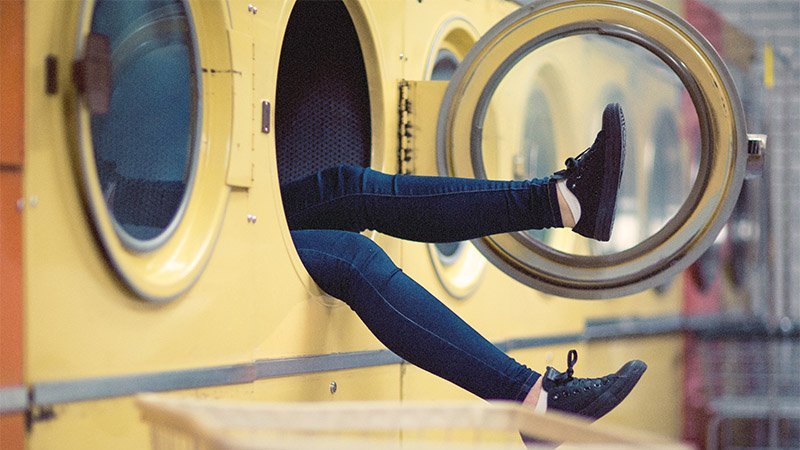 Geldwäsche: Zwei Beine schauen aus einer Waschmaschine heraus