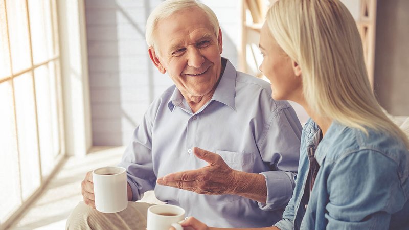 älterer Herr und junge Frau sitzen zusammen und trinken Kaffee