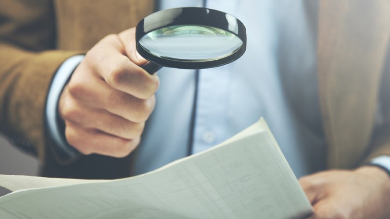 Ein Mann schaut mit einer Lupe auf ein Blatt Papier