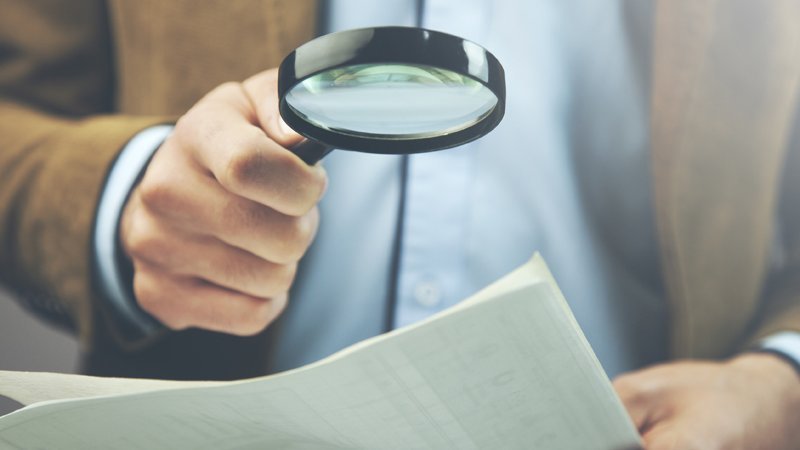 Ein Mann schaut mit einer Lupe auf ein Blatt Papier